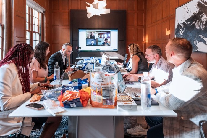 Team collaborating in an office meeting with laptops and a video conference screen.